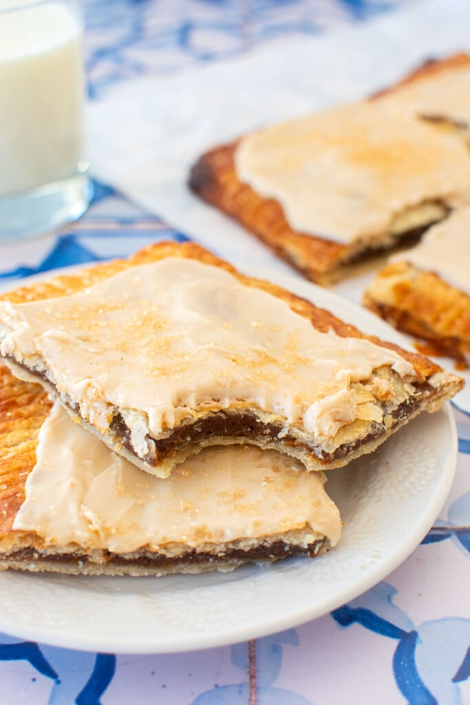 two pumpkin spice pop tarts on a plate with a glass of milk on a blue tile table.
