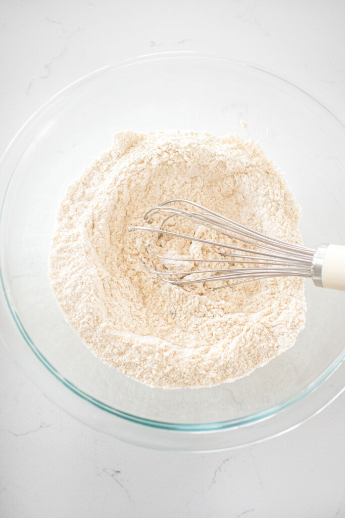 dry ingredients mixed together with a whisk for eggnog waffles in a glass mixing bowl on a white marble counter.