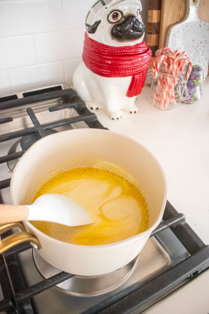 melted butter in a small pot on the stovetop being stirred with a spatula.