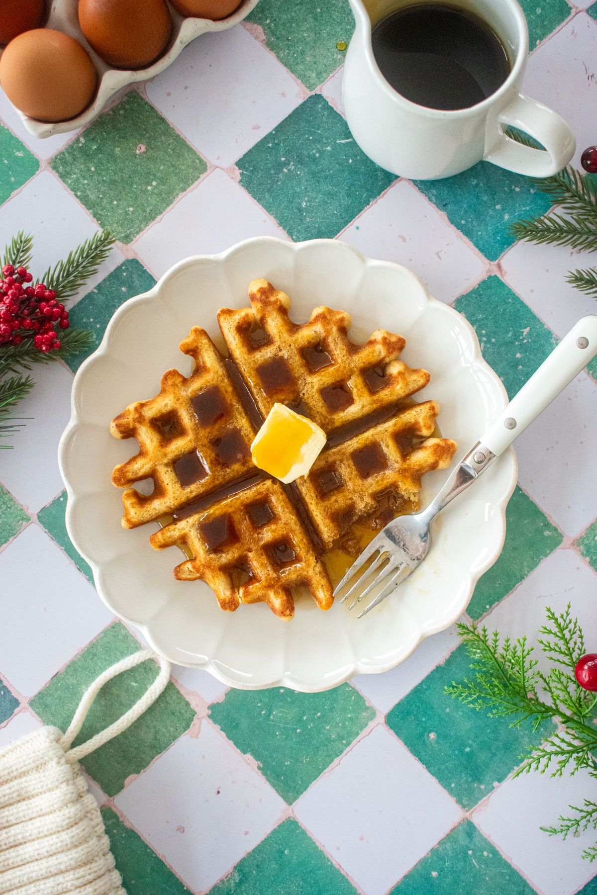 homemade eggnog waffles on a plate with butter and maple syrup on a green tile table.