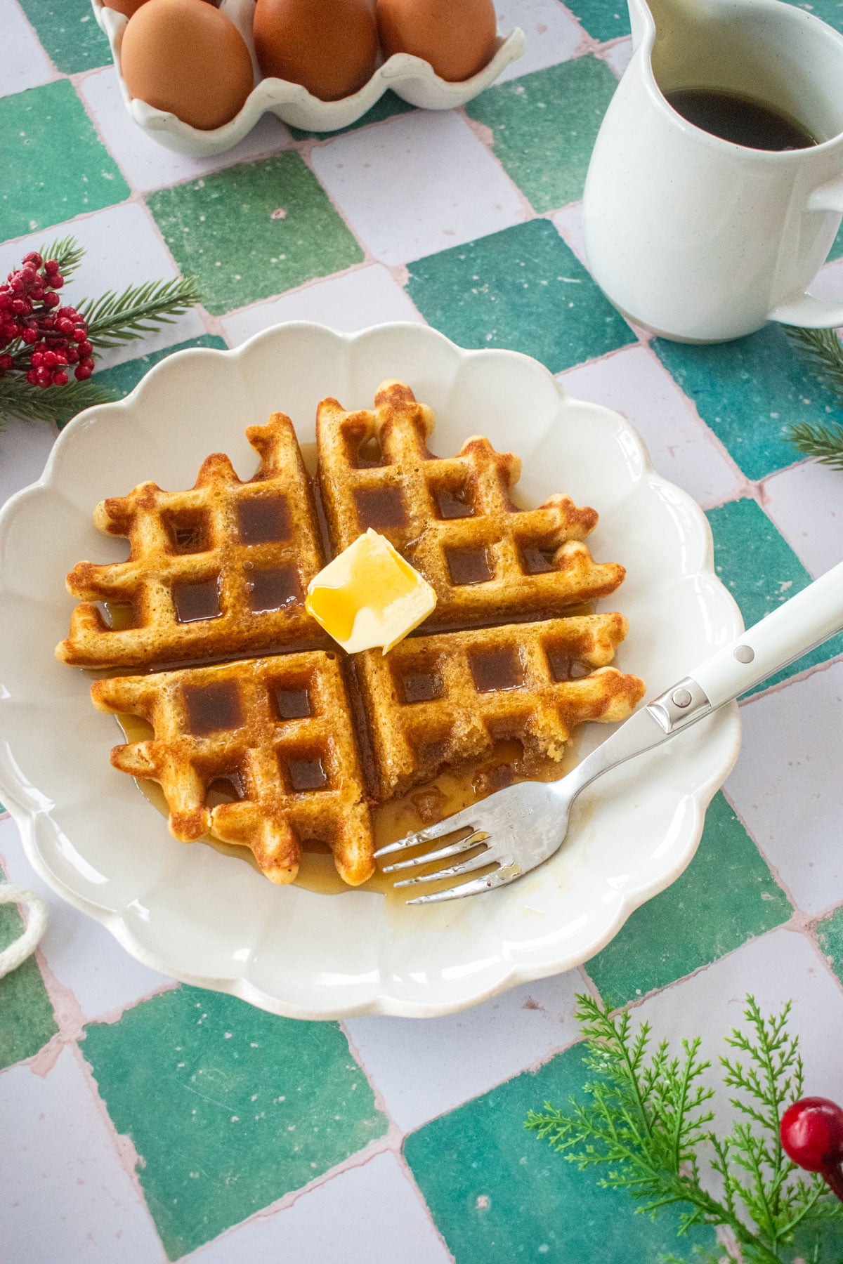 homemade eggnog waffles on a plate with butter and maple syrup on a green tile table.