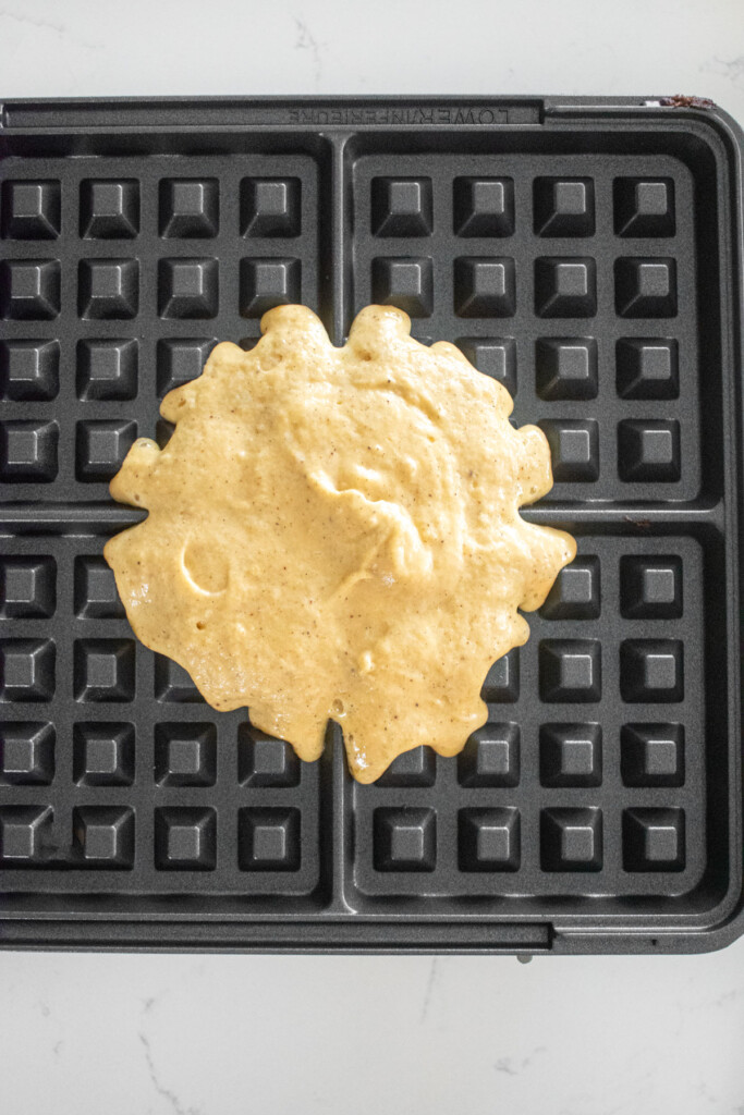 eggnog waffle batter in a waffle iron on a white marble counter.