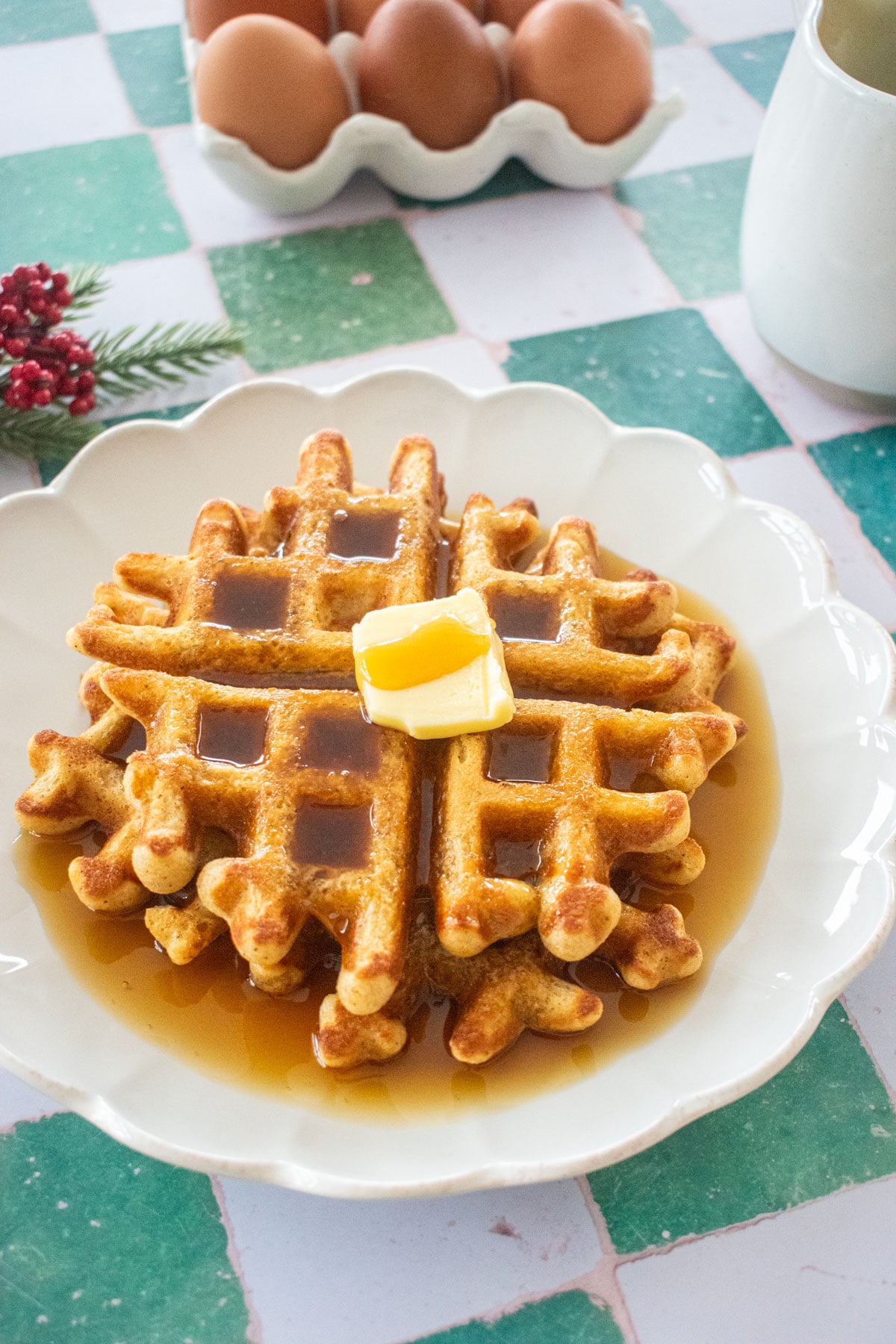 homemade eggnog waffles on a plate with butter and maple syrup on a green tile table.