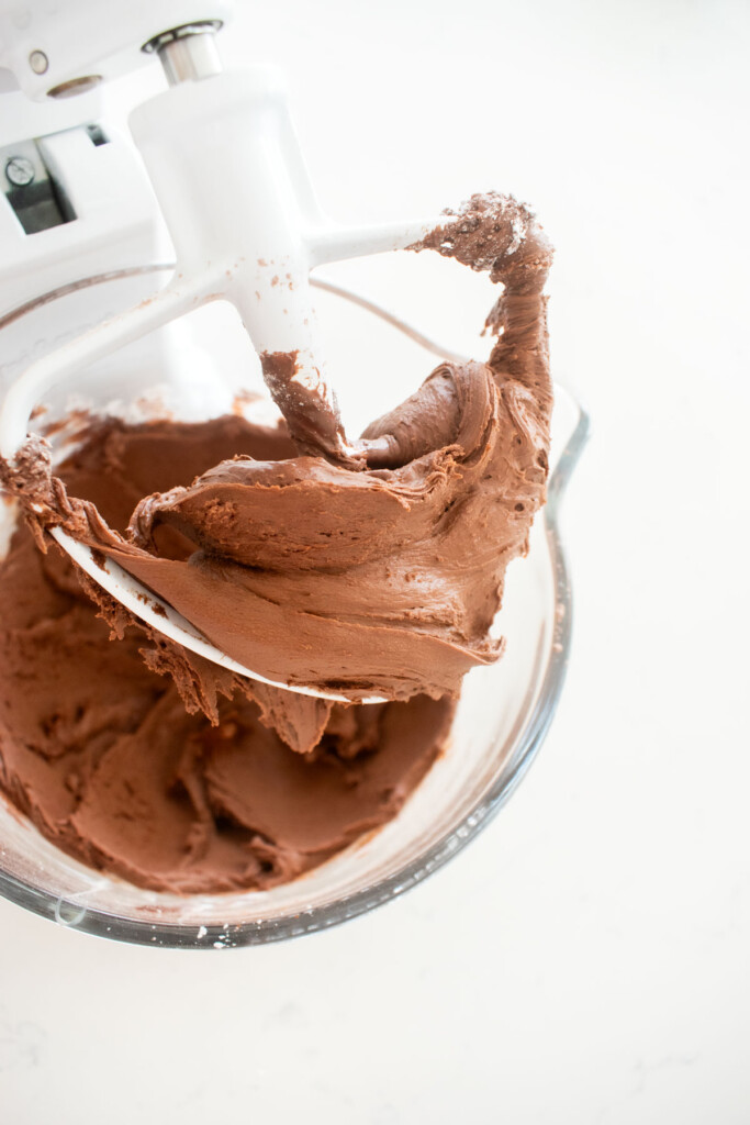 mint meltaways being mixed in a glass stand mixing bowl on a white marble counter.