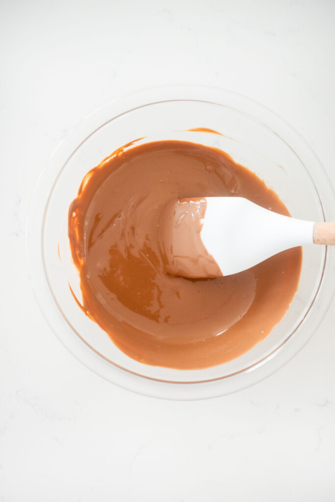 melted milk chocolate in a glass mixing bowl on a white marble counter.