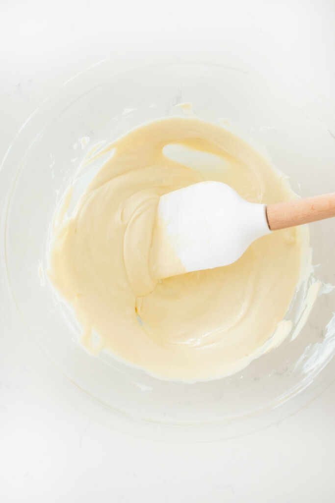 melted white chocolate in a glass mixing bowl on a white marble counter.