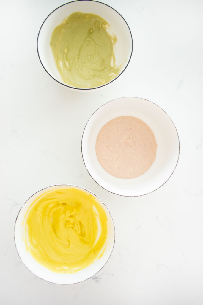 three bowl of white chocolate colored pastel green, pink, and yellow on a white marble counter.