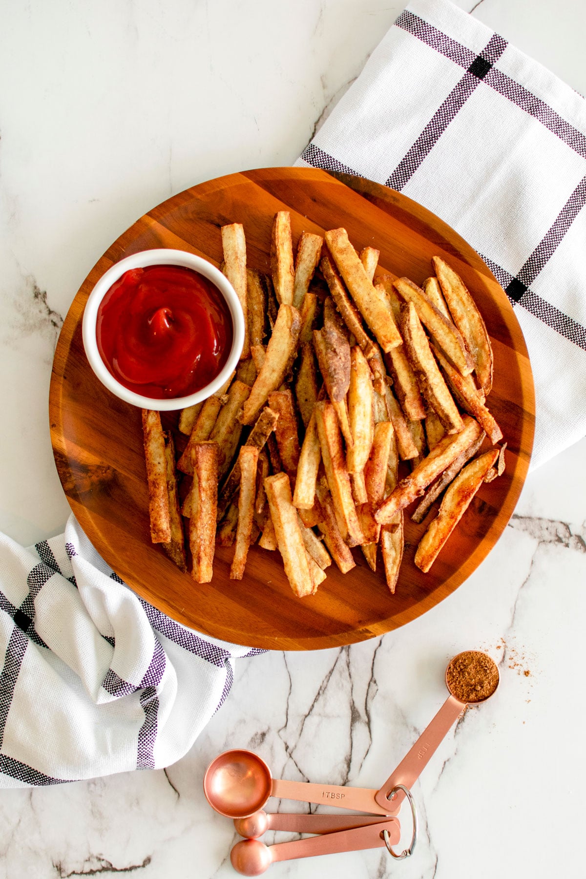 chinese five spice garlic french fries on a wood plate with a small dish of ketchup on a marble countertop.