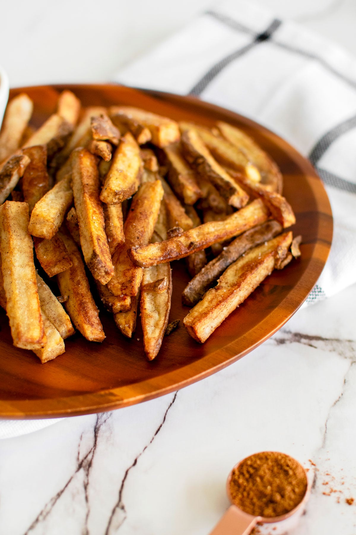 chinese five spice garlic french fries on a wood plate on a white marble countertop.