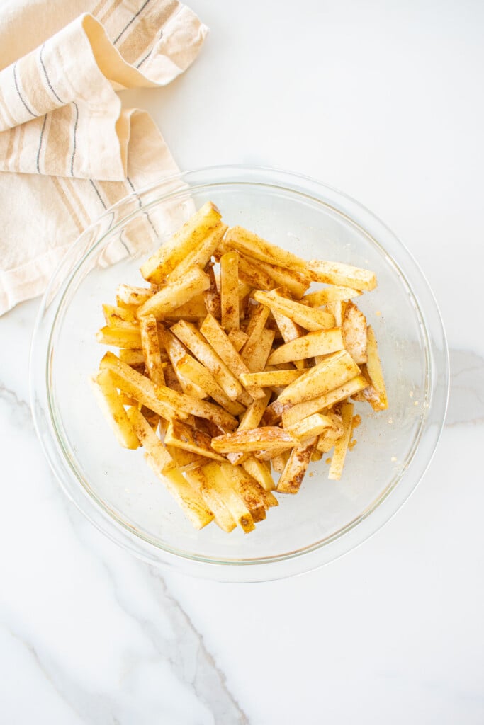chinese five spice garlic fries mixed withs seasoning in a glass mixing bowl on a marble counter.