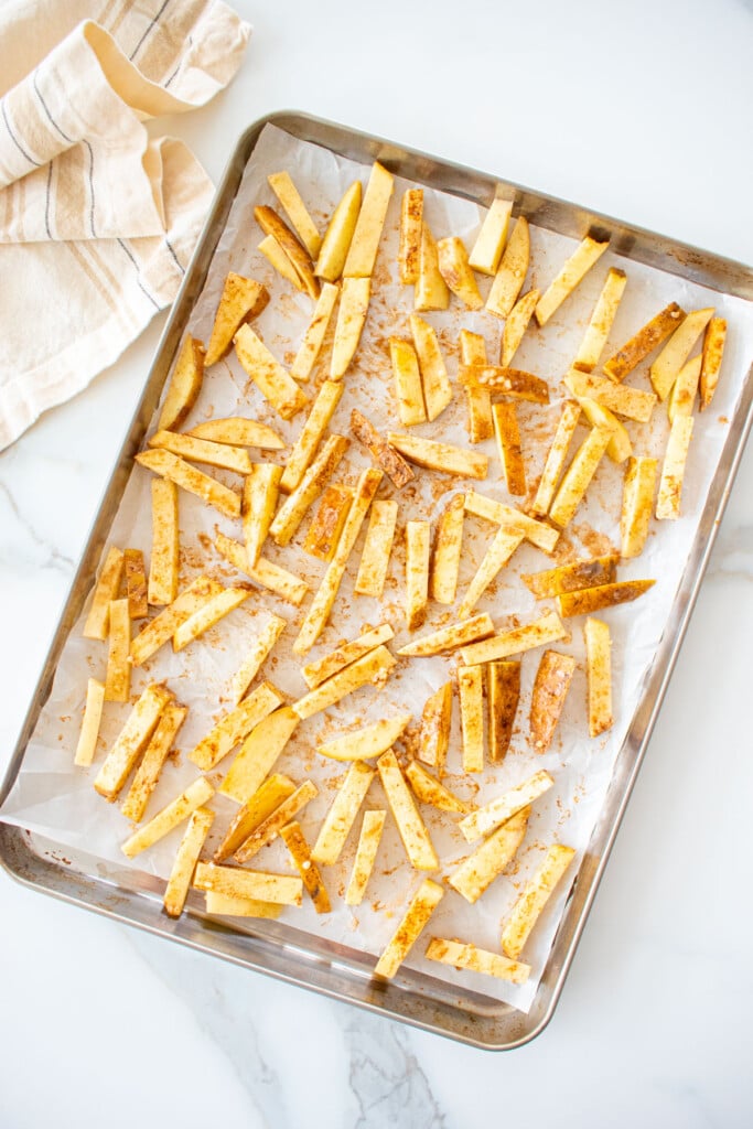 a baking sheet with raw chinese five spice garlic fries spread out evenly on a marble counter.