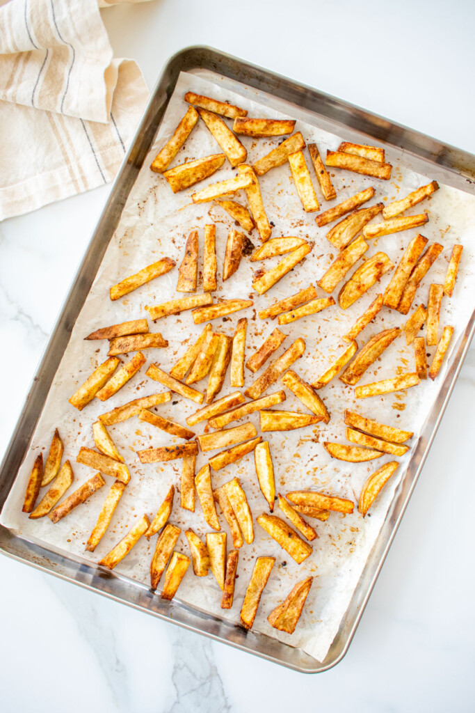 a baking sheet with baked chinese five spice garlic fries spread out evenly on a marble counter.