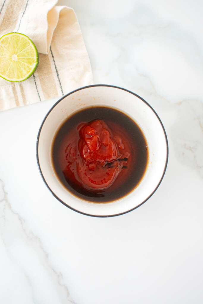 bowl with ketchup, coconut aminos and lime juice on a marble counter.