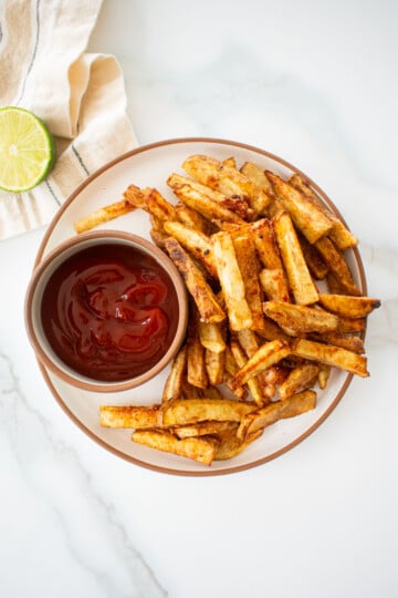 plate with chinese five spice garlic fries on a plate with soy lime ketchup in a small bowl on a marble counter.