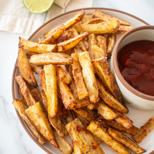 plate with chinese five spice garlic fries on a plate with soy lime ketchup in a small bowl on a marble counter.