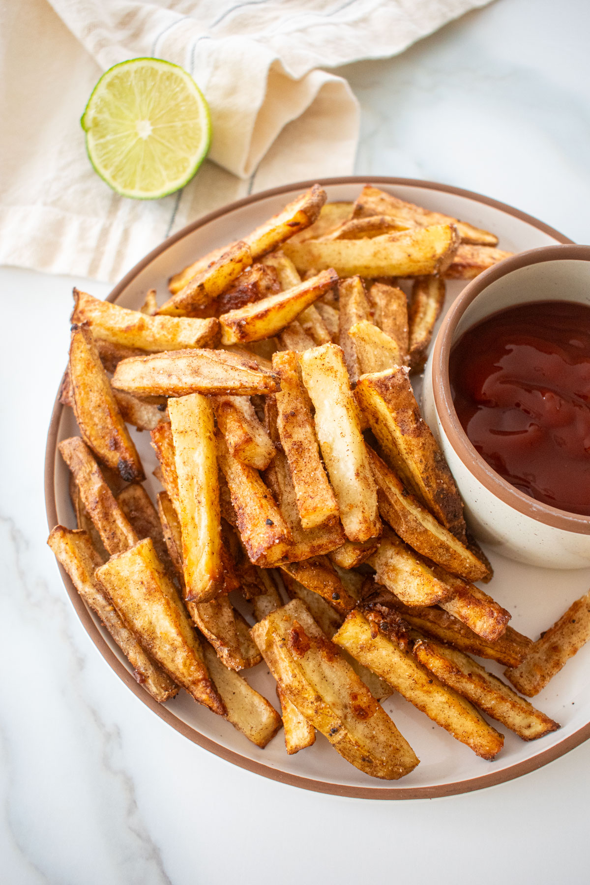 plate with chinese five spice garlic fries on a plate with soy lime ketchup in a small bowl on a marble counter.