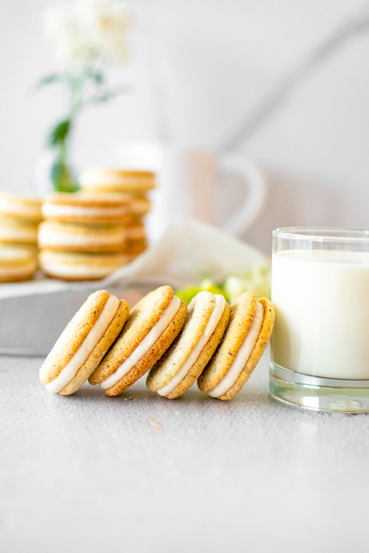 earl grey sandwich cookies stacked leaning on a glass of milk on a gray countertop.