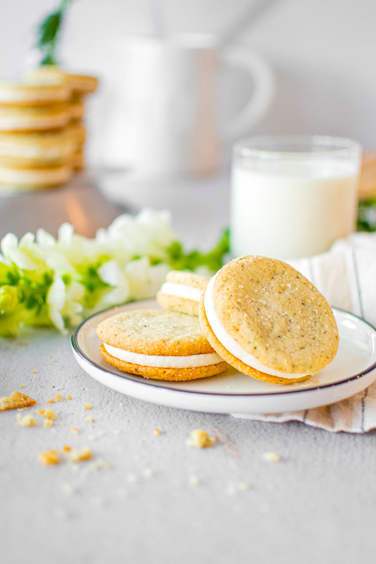 plate of earl grey sandwich cookies on a grey counter with fresh flowers.