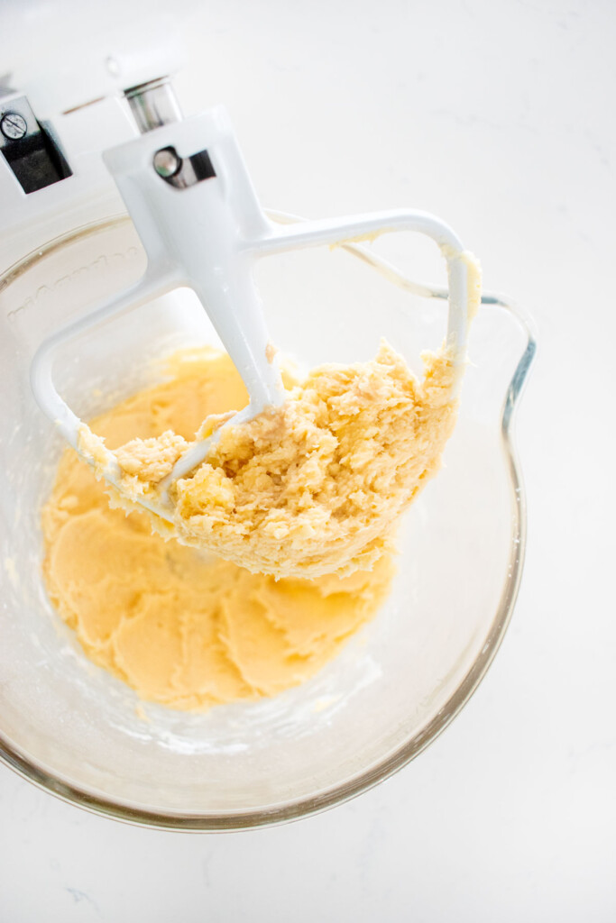 creamed butter and powdered sugar in a glass stand mixing bowl on a white marble counter.