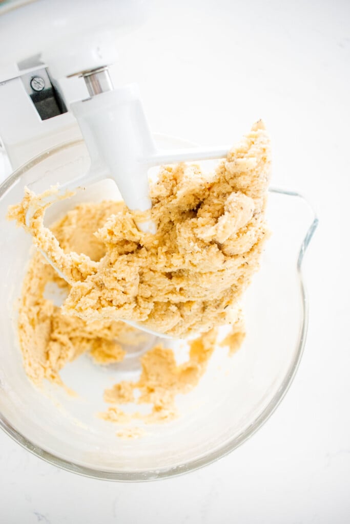earl grey shortbread cookie dough in a glass stand mixing bowl on a white marble counter.
