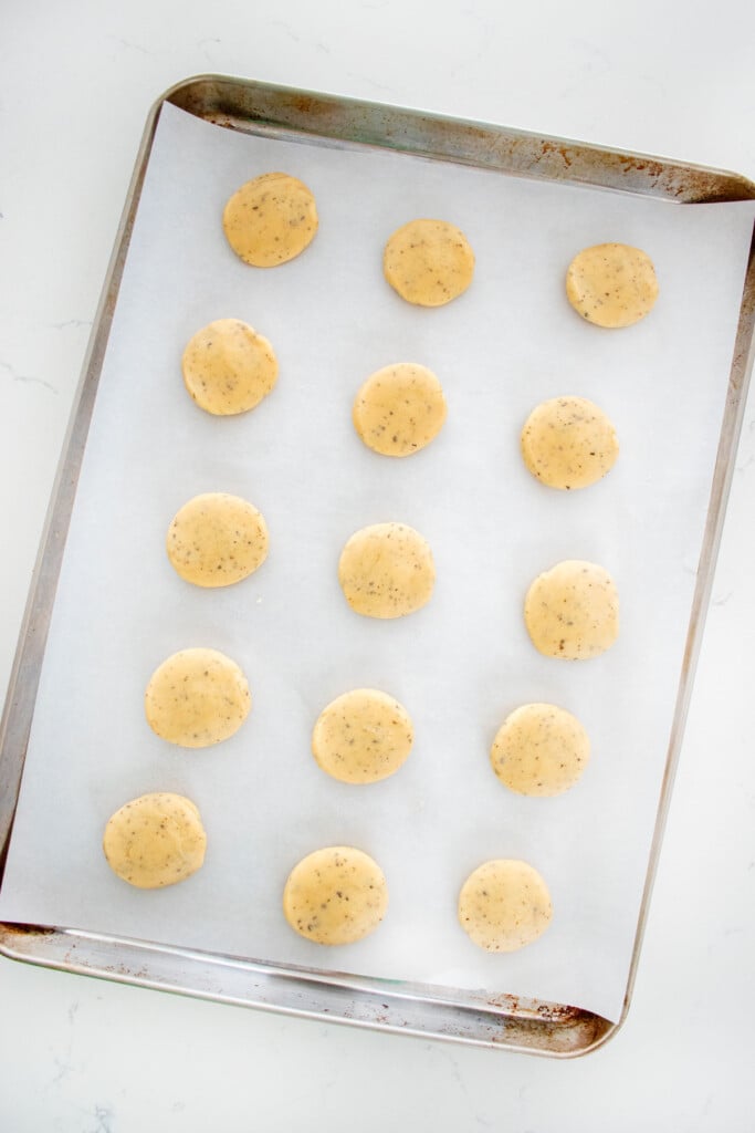 earl grey shortbread cookie dough balls on a baking sheet on a white marble counter.