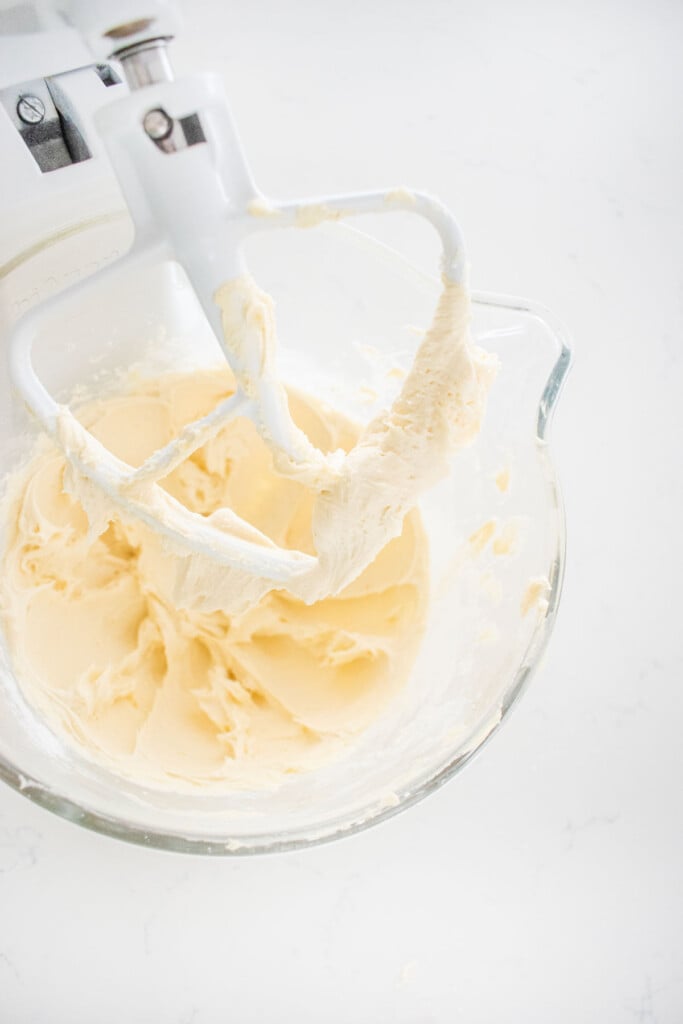 buttercream frosting in a glass stand mixing bowl on a white marble counter.