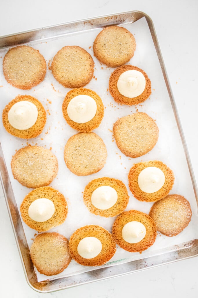 earl grey sandwich cookies being filled with buttercream frosting on a baking sheet on a marble counter.