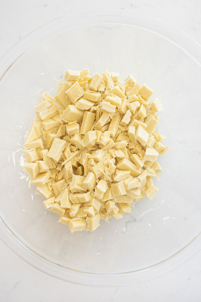 white chocolate chunks in a glass mixing bowl on a marble counter.