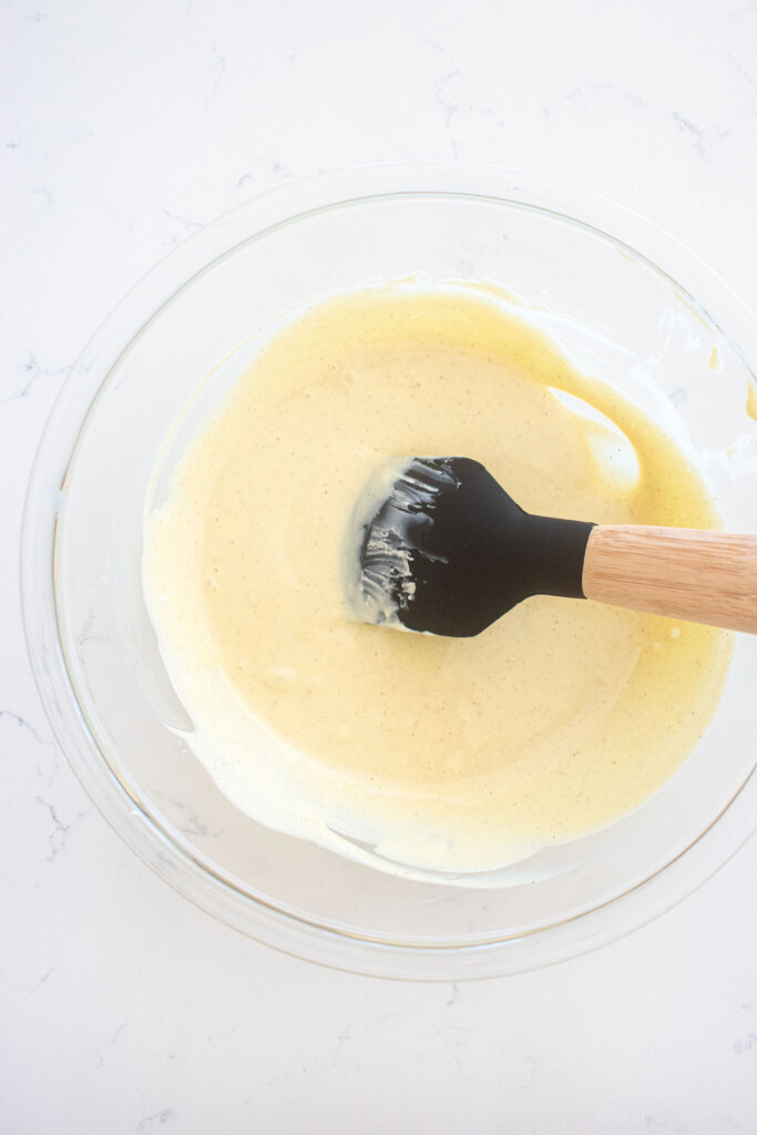melted white chocolate in a glass mixing bowl on a marble counter.