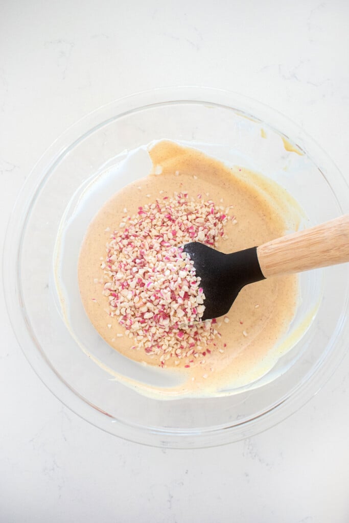 pink white chocolate in a glass mixing bowl with peppermint crunch on a marble counter.