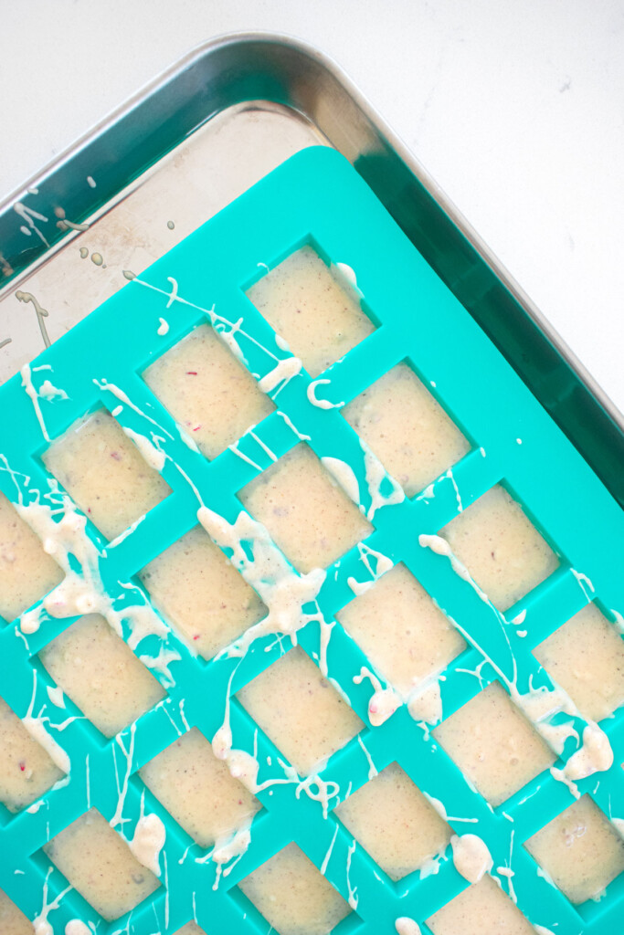 candy mold on a baking sheet with pink peppermint ice on a marble counter.