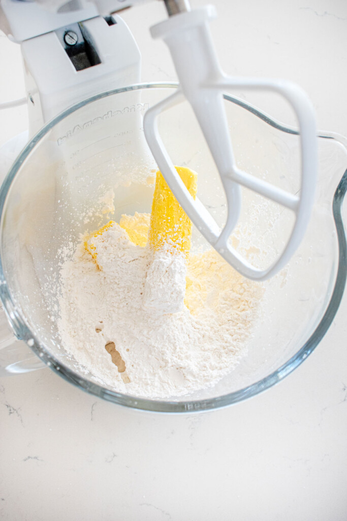 butter powdered sugar and peppermint extract in a glass mixing bowl on a marble counter.