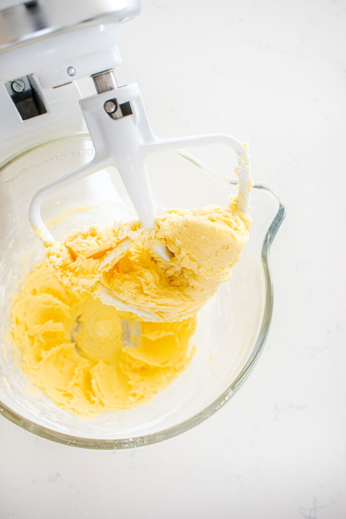 creamed butter and powdered sugar in a glass mixing bowl on a marble counter.