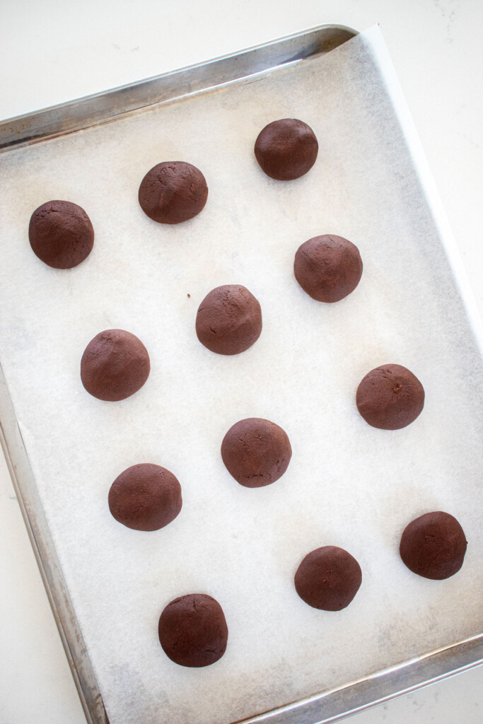 chocolate cookie dough balls on a baking sheet on a marble counter.