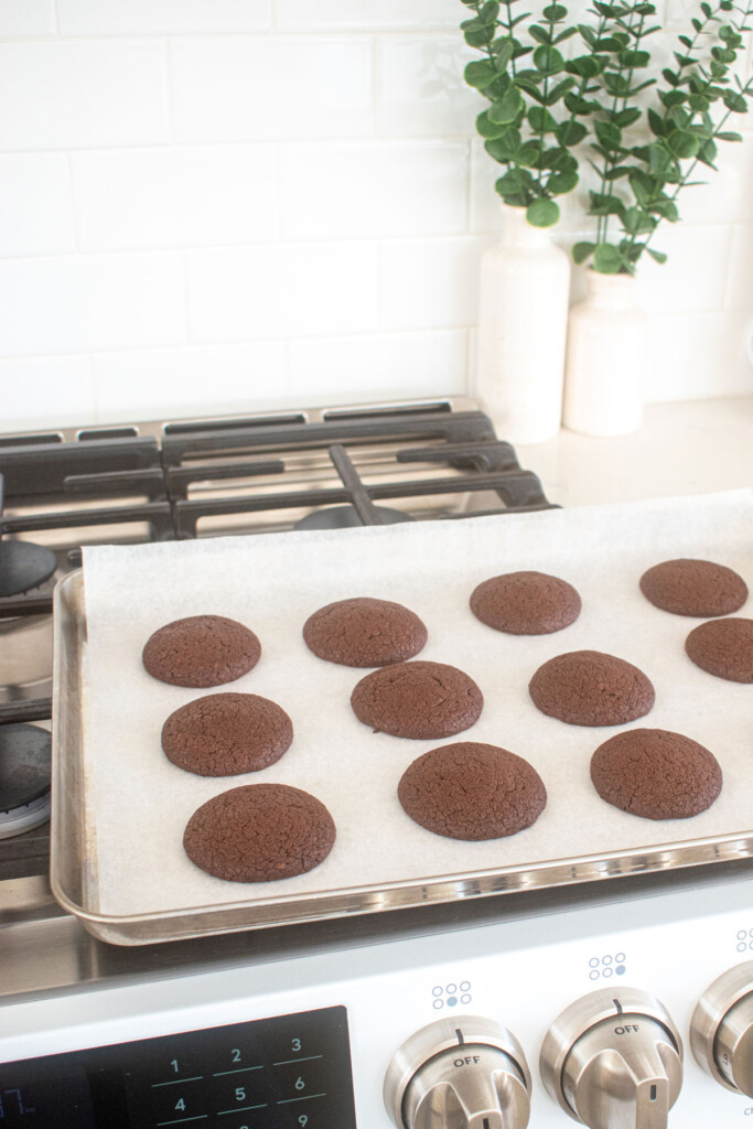 baked chocolate cookies on a baking sheet cooling on top of the oven.