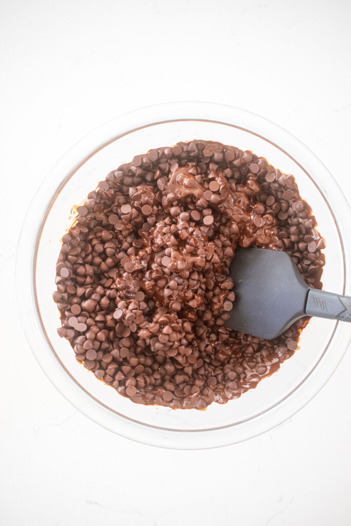 chocolate chips being melted in a glass mixing bowl on a marble counter.