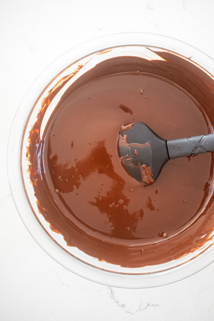 melted dark chocolate in a glass mixing bowl on a marble counter.