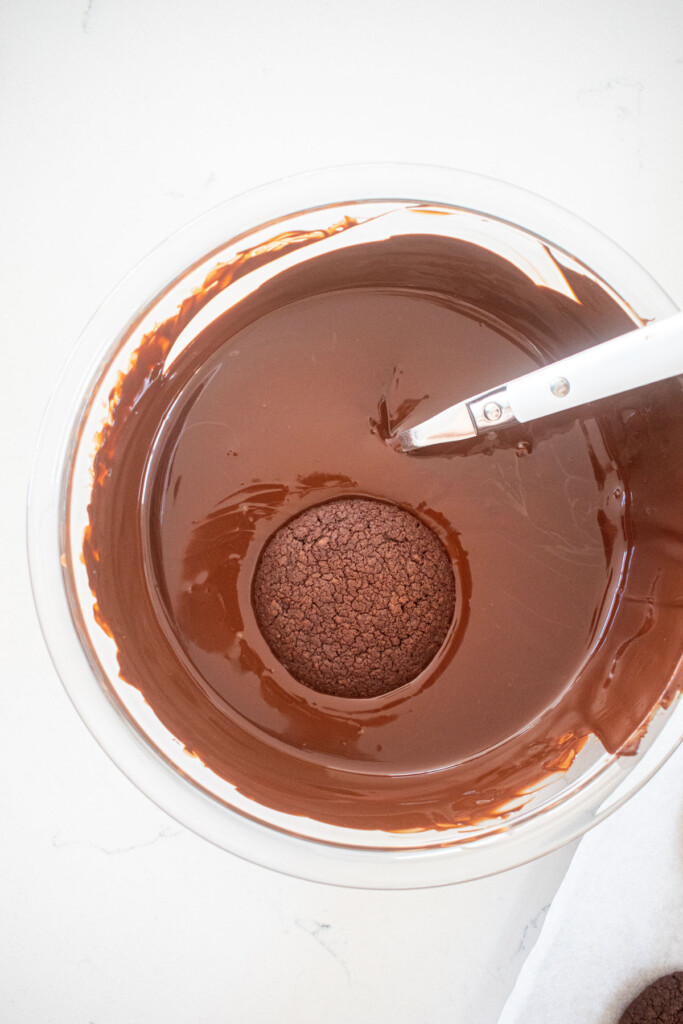 thin mint cookie in a bowl of melted dark chocolate on a marble counter.
