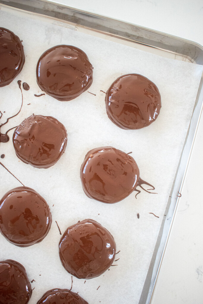 homemade thin mint cookies covered in chocolate on a baking sheet on a marble counter.