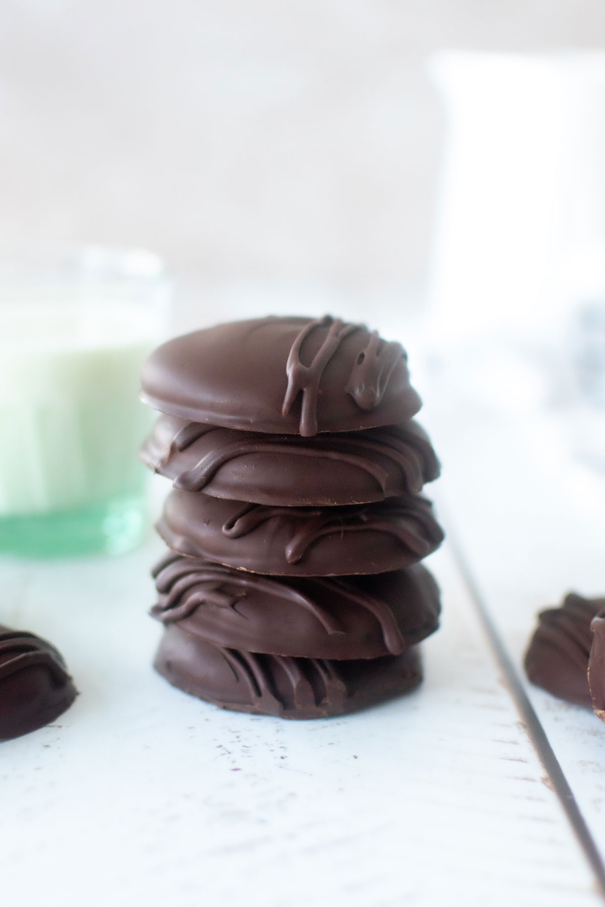 stack of homemade organic thin mint cookies on a white wood table with a glass of milk.