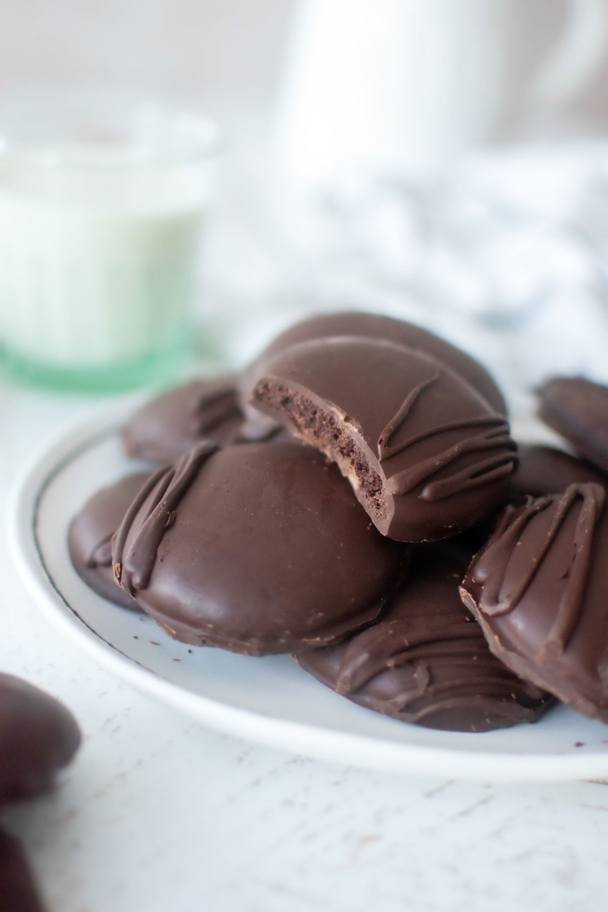 homemade organic thin mint cookies on a plate with a glass of milk on a white wood table.