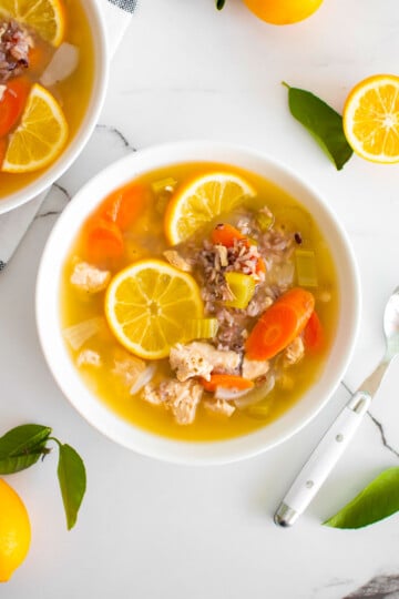 meyer lemon chicken and wild rice soup in a white soup bowl on a white marble countertop.
