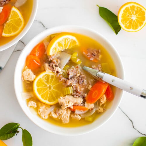 meyer lemon chicken and wild rice soup in a white soup bowl on a white marble countertop.