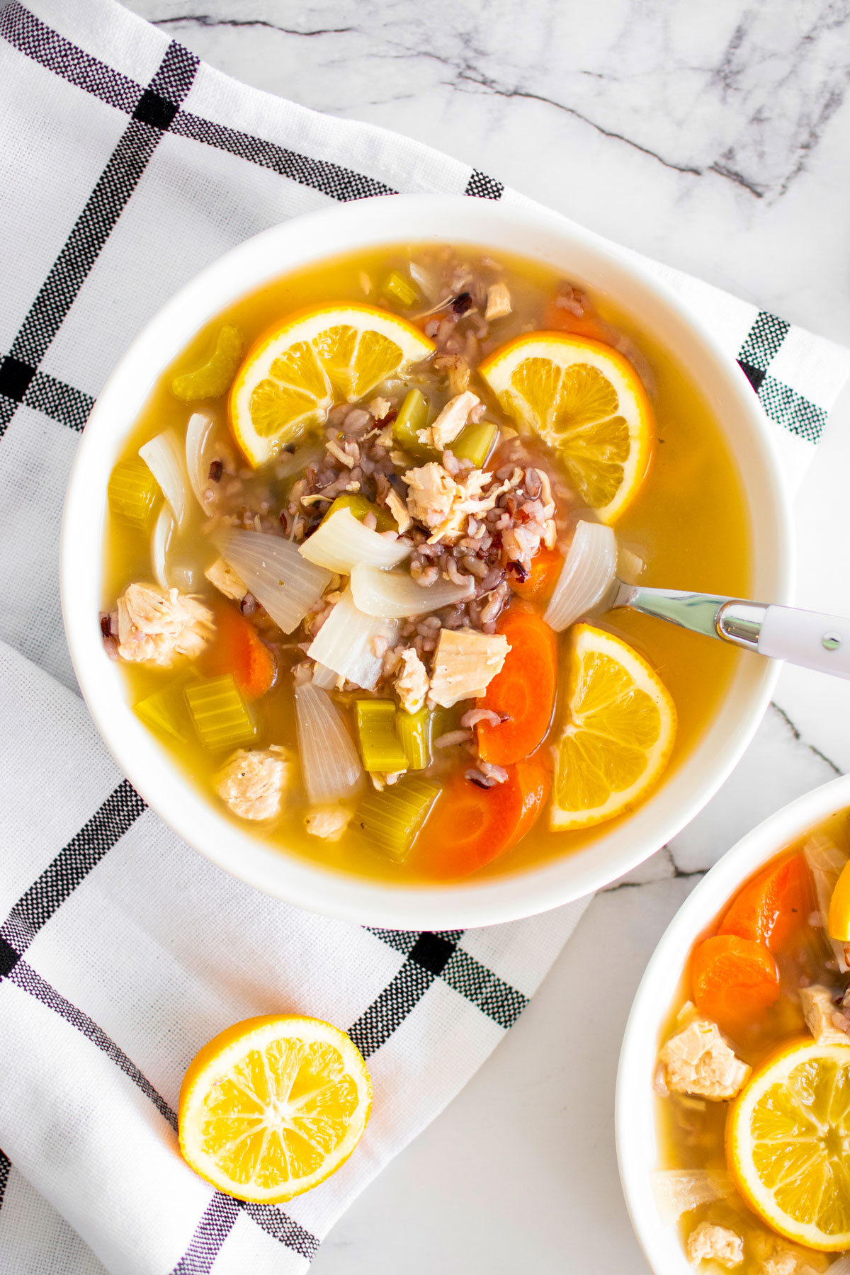 meyer lemon chicken and wild rice soup in a white soup bowl on a white marble countertop.