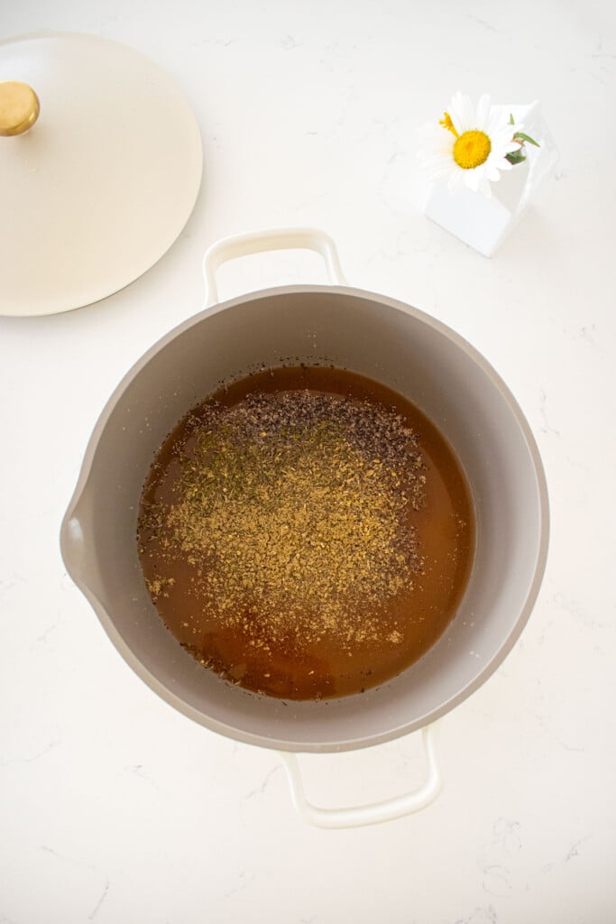 dutch oven on a marble counter with bone broth and spices.