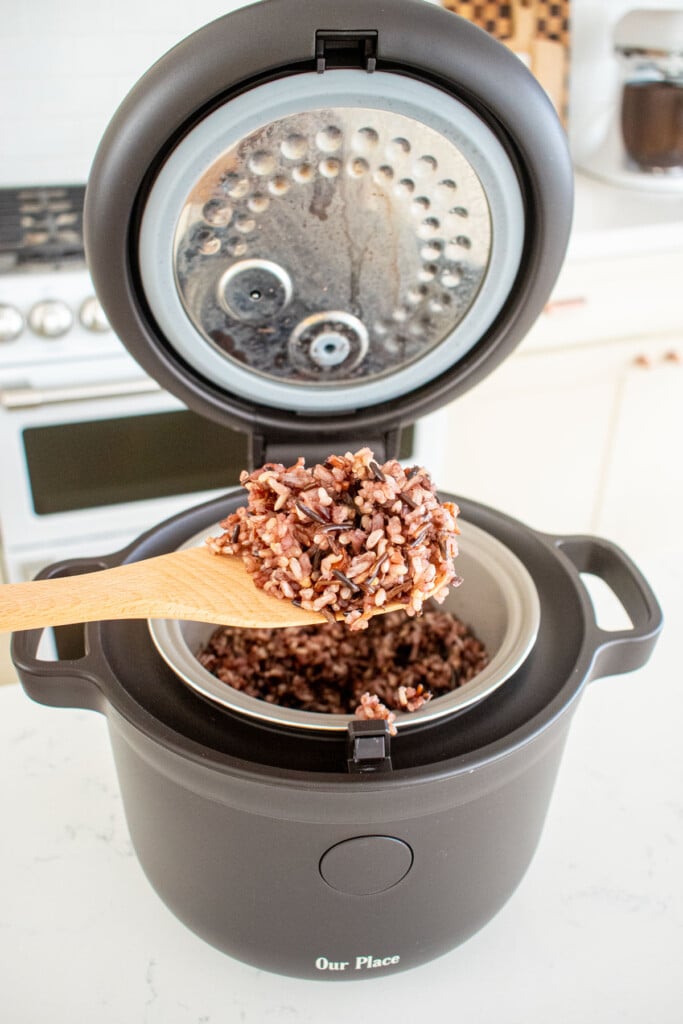 rice cooker with cooked wild rice on a wood rice paddle on a marble counter.