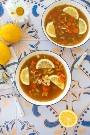 meyer lemon chicken wild rice soup with bone broth in big soup bowls on a tile table with fresh lemons and flowers.