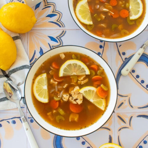meyer lemon chicken wild rice soup with bone broth in big soup bowls on a tile table with fresh lemons and flowers.