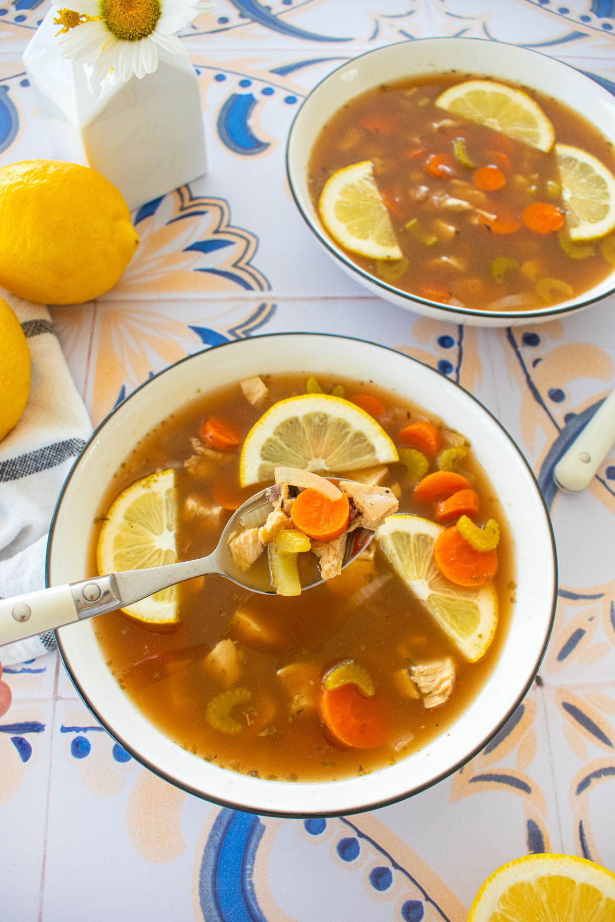 meyer lemon chicken wild rice soup with bone broth in big soup bowls on a tile table with fresh lemons and flowers.