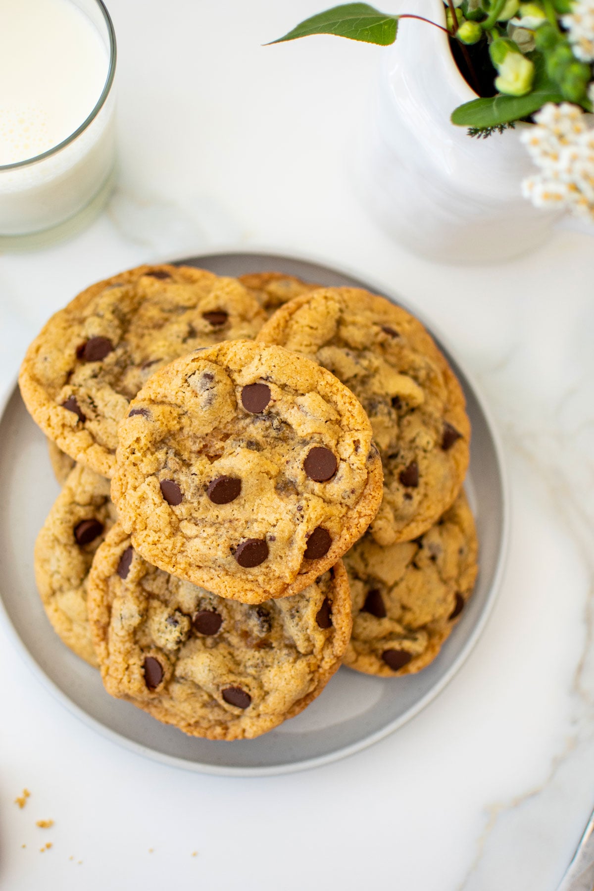 eggless chocolate chip cookies on a plate with a glass of milk on a white marble counter.